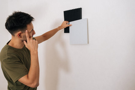 Thoughtful male comparing different soundproofing acoustic panels and placing them on wall for noise...