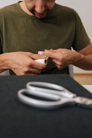 Vertical shot of young man applying medical patch to injured finger, demonstrating self-care for...
