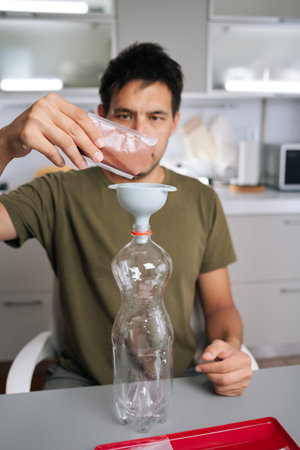 Vertical portrait of gardener male pouring organic fertilizer through funnel into mixing bottle,...
