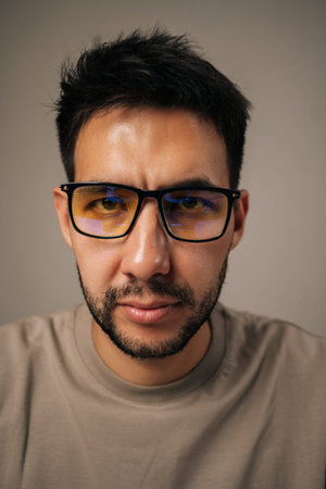 Close-up vertical portrait of young man wearing anti-fatigue glasses with focused and concerned...