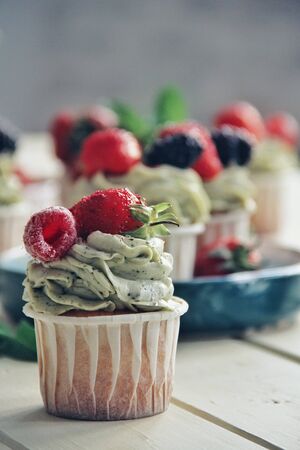 Strawberry creamy cupcakes and green leaves, mint with flowers on white wooden kitchen background. Sweets for breakfest. Tasty food, beauty of delicious and art concept. Juicy colors, seasonal snack.の写真素材