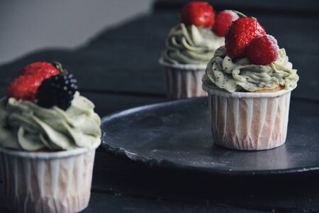 Strawberry creamy cupcakes with mint on black wooden kitchen background. Sweets for breakfest. Tasty food, beauty of delicious and art concept. Juicy colors, seasonal snack.の写真素材
