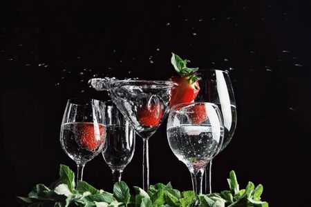 White martini cocktails splashing with drops into glasses on black background with strawberries inside it and mint leaves. Alcohol drinks, friend's time, chill, resort. Beauty or food and drinks.の写真素材