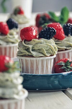 Strawberry creamy cupcakes and green leaves, mint with flowers on white wooden kitchen background. Sweets for breakfest. Tasty food, beauty of delicious and art concept. Juicy colors, seasonal snack.の写真素材
