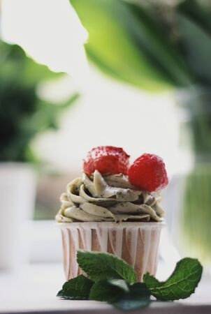 Strawberry creamy cupcake and green leaves, mint with flowers on white wooden kitchen background. Sweets for breakfest. Tasty food, beauty of delicious and art concept. Juicy colors, seasonal snack.の写真素材