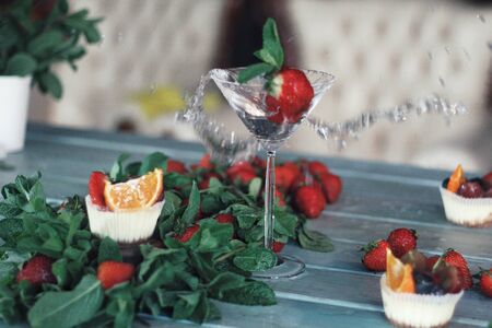 Strawberry creamy cupcakes and green leaves, mint, splashing drink on white wooden kitchen background. Sweets, breakfest. Tasty food, beauty of delicious and art concept. Juicy colors, seasonal snack.の写真素材