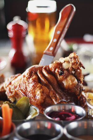 Pork knuckle with carrot, cucumber, sauce and light filtered beer on the pub's table background. Tasty drinks and food. Oktoberfest traditions, delicious snacks, festival, alcohol, friend's time.の写真素材