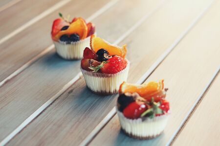 Strawberry creamy cupcakes and green leaves, mint with flowers on white wooden kitchen background. Sweets for breakfest. Tasty food, beauty of delicious and art concept. Juicy colors, seasonal snack.の写真素材