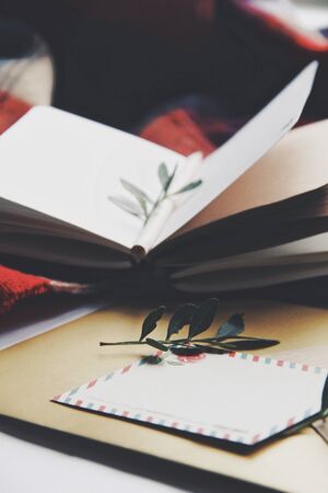 Opened book, green leaves, greeting postcard. Autumn home comfort, warm light. Evening or holidays atmosphere in family house. Time for greeting those who loves you. Holiday wishes, romantic. Flatlay.の写真素材