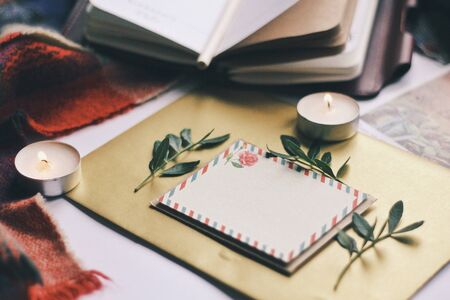 Opened book, green leaves, greeting postcard and candles. Autumn home comfort, warm. Evening atmosphere in family house. Time for greeting those who loves you. Holiday wishes, romantic. Flatlay.の写真素材