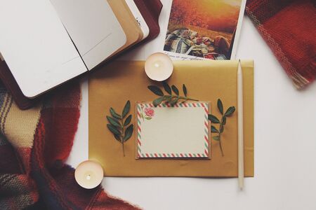 Opened book, green leaves, greeting postcard and candles. Autumn home comfort, warm. Evening atmosphere in family house. Time for greeting those who loves you. Holiday wishes, romantic. Flatlay.の写真素材