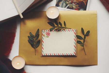 Opened book, green leaves, greeting postcard and candles. Autumn home comfort, warm. Evening atmosphere in family house. Time for greeting those who loves you. Holiday wishes, romantic. Flatlay.の写真素材