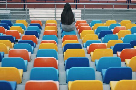 Sensual portrait of beautiful young girl walking in the old abandoned stadium on cold autumn day. Caucasian female model sitting on arena. Human emotions, facial expression, fashion, sport, lifestyle.の写真素材