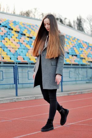 Sensual portrait of beautiful young girl walking in the old abandoned stadium on cold autumn day. Caucasian female model in front of sits. Human emotions, facial expression, fashion, sport, lifestyle.の写真素材