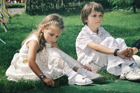 Portrait of little caucasian girl and boy in casual clothes sitting on grass. Cute friends or sister and brother looks dreamful. Happy childhood, art, family, freinds, relation concept. Pure emotions.の写真素材
