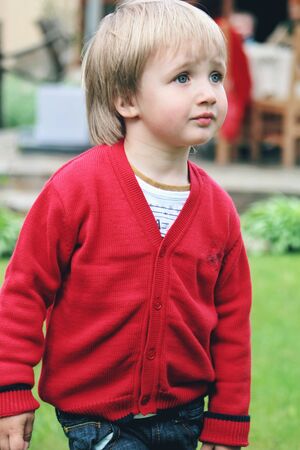 Portrait of little caucasian boy in casual clothes at home garden. Cute male model smiling, posing, looking at side confident on grass background. Childhood, art, style, beauty and fashion concept.の写真素材