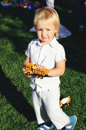 Kissed by sun. Portrait of little caucasian boy playing with toys in garden. Cute male model plays game, looks happy. Childhood, art, style, beauty, fashion concept. Human emotions. Sunlight.の写真素材