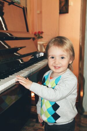 Lovely musician. Portrait of little caucasian boy playing piano at home. Cute male model plays music, looks happy, astonished, laughting. Childhood, art, style, beauty, fashion concept. Human emotions.の写真素材