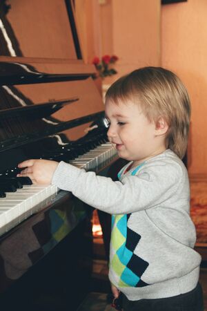 Sound of happiness. Portrait of little caucasian boy playing piano at home. Cute male model plays music, looks happy, laughting. Childhood, art, style, beauty, fashion concept. Human emotions.の写真素材