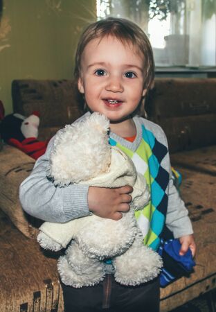 My best friend. Portrait of little caucasian boy playing with toys at home. Cute male model plays game, looks happy, holding teddy bear. Childhood, art, style, beauty, fashion concept. Human emotions.の写真素材