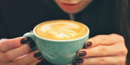 Caucasian young woman enjoying coffee drinking in cafe, close upの写真素材