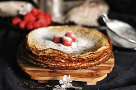 Thin crepes, pancakes or blinis with strawberry and chocolate on slate on black background, tasty...