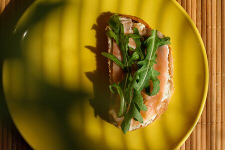 Sandwich with smoked salmon, butter and parsley. Concept of healthy nutrition. Tasty fish on bread on yellow plate in sunlight, warm and appetizer. Healthy food, dieting, meal and cuisine, lunch.の写真素材