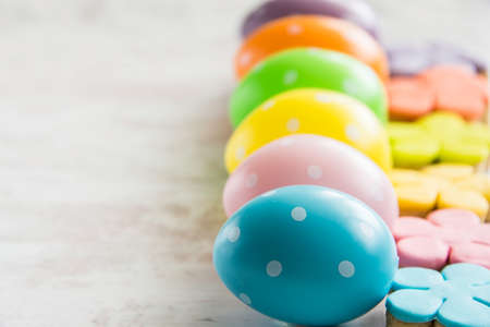 Colorful easter eggs with flower cut homemade cookies on a white wood backgroundの写真素材