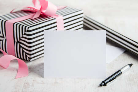 Empty greeting card with a pen. Wrapped gift and wrapping paper roll in the background.の写真素材