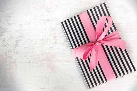 Gift box wrapped in black and white striped paper with pink ribbon on a white wood old backgroundの写真素材
