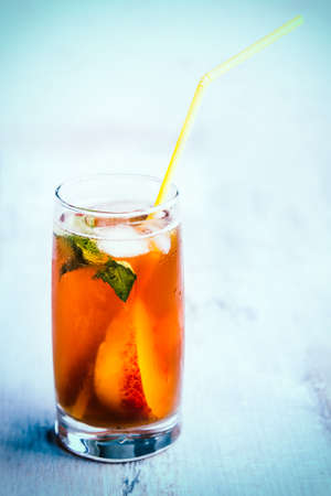 A glass with homemade ice tea, peach flavored. Freshly cut peach slices for arrangement. Light blue wood background. background.の写真素材