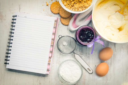 Empty recipe notebook with cheese cake ingredients prepared over a white wood background.の写真素材