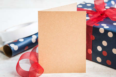 Empty greeting kraft card. Wrapped gift and wrapping materials over a white wood background.の写真素材