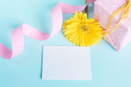 Pink dotted gift box, yellow gerbera flower and empty card over a blue background.の写真素材