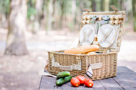 Open picnic basket with tomatoes, cucumbers and bread over a wooden table in the park.の写真素材