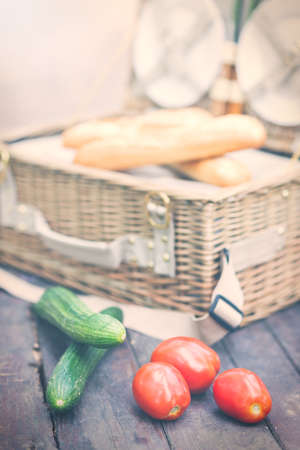 Close up of tomatoes and cucumbers over wooden table in front of an open picnic basket.の写真素材