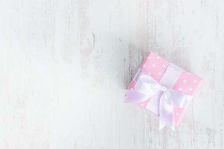 Top view of a gift box wrapped in pink dotted paper and tied satin bow over a white wood background.の写真素材