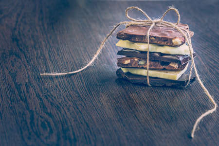 A tower of chocolate bars wrapped like a chocolate present . Various chocolate pieces over dark wood background.の写真素材