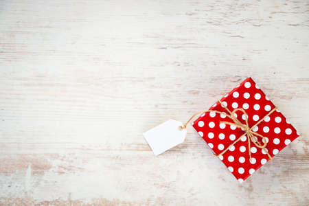 Top view of a red dotted gift box over white wood background. Copy space. Empty note.の写真素材