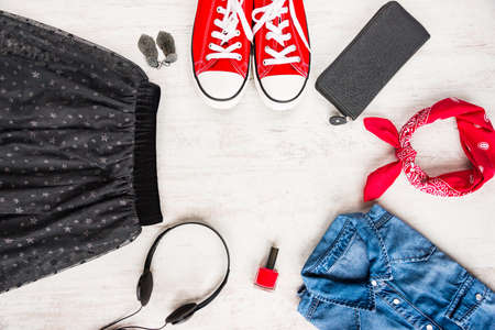 Top view of yong woman clothes and accessories. Tulle skirt, denim shirt, wallet, head phones, earrings, nail polish, sneakers and kerchief. Urban style concept.の写真素材