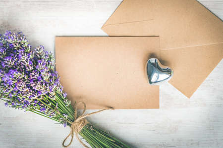 Top view of an empty greeting kraft card and envlope, lavender bouquet and silver heart over white...