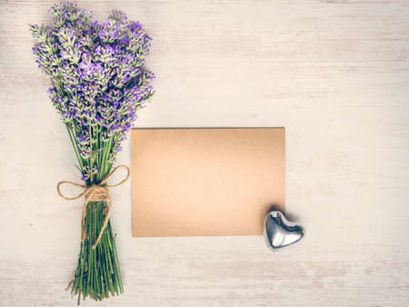 Top view of an empty greeting kraft card, lavender bouquet and silver heart over white wood rustic wooden table. Kraft mockup.の写真素材