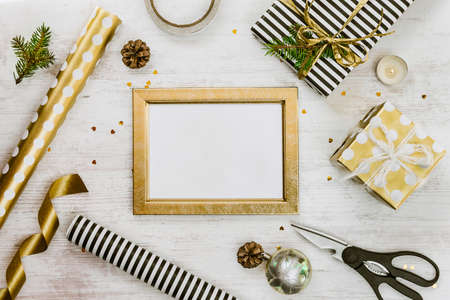 Golden ptoto frame, gift boxes, pine cones and christmas toys and wrapping materials on a white wood old background. Christmas concept. Frame mock up.の写真素材