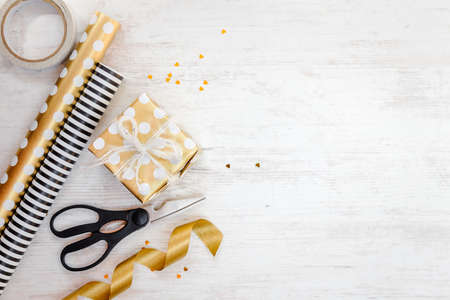 Gift box wrapped in golden dotted paper and wrapping materials on a white wood old background. Empty space.の写真素材