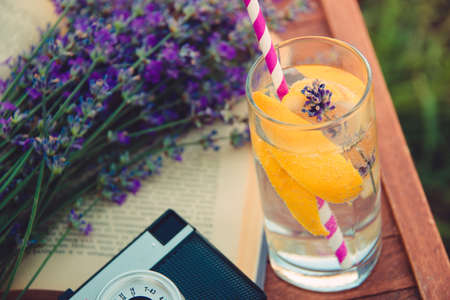 A glass of refreshing lemonade, vintage cameta, a book and freshly cutted lavender flowers over a wooden chair.の写真素材