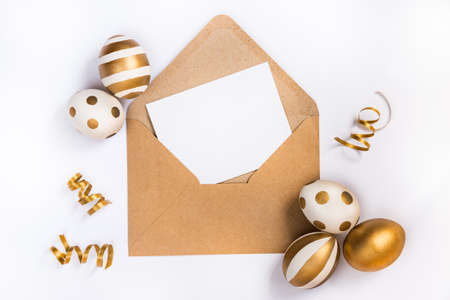 Easter festive decoration. Top view of easter eggs colored with golden paint in differen patterns and empty mock-up card in a kraft envelope. Various striped and dotted designs. White background.の写真素材