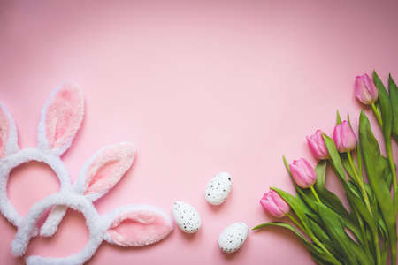 Top view of Easter eggs, pink tulips and two white fluffy bunny ears over pink background. Easter concept background.Copy space.の写真素材