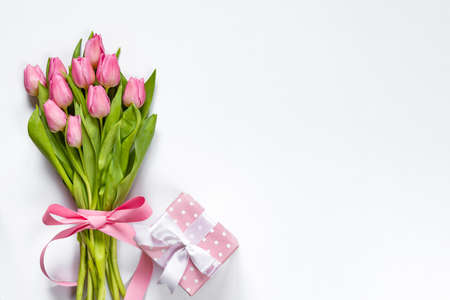 Top view of pink tulips bouquet, wrapped with pink ribbon and pink dotted gift box over white background. Copy space.の写真素材