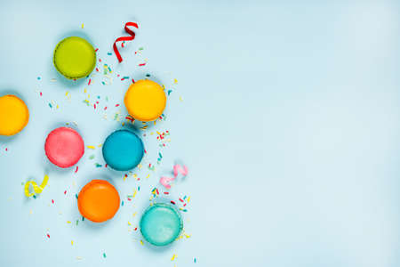 Top view of colorful macaroons, sugar sprinkles and party ribbons arranged over blue background. Copy space.の写真素材