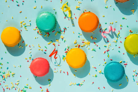 Top view of colorful macaroons, sugar sprinkles and party ribbons over blue background. Abstract party food background.の写真素材